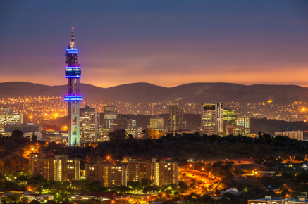Pretoria city skyline at dusk with the Telkom Tower illuminated and the Magaliesberg mountain range in the background